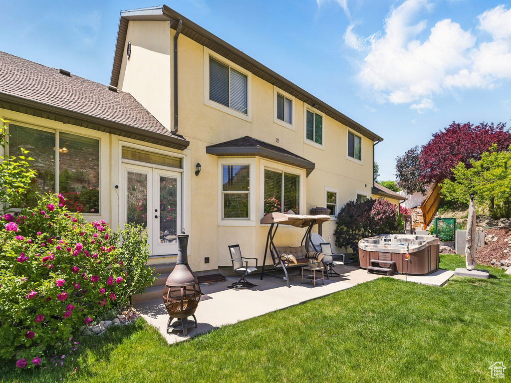 Back of property featuring a hot tub, stucco siding, a patio, a lawn, and french doors