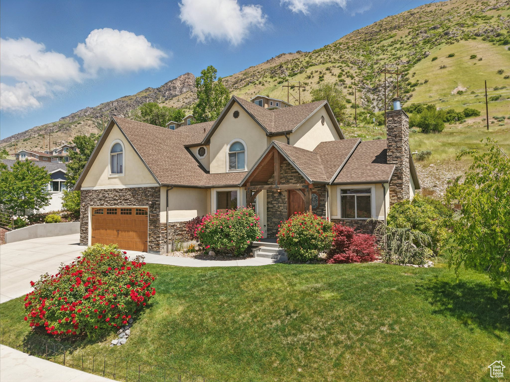 View of front facade with stucco siding, stone siding, a chimney, concrete driveway, and a mountain view