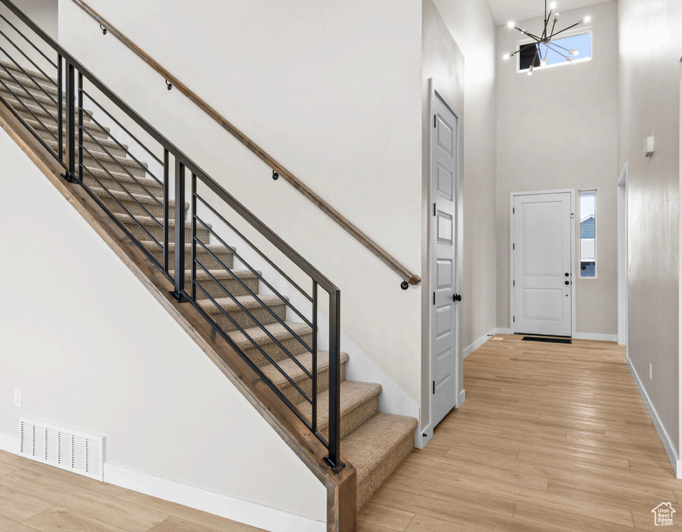 Foyer with a towering ceiling, baseboards, stairs, a chandelier, and light wood-type flooring