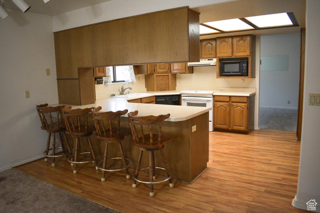 Kitchen featuring black appliances, a peninsula, light wood-style floors, light countertops, and brown cabinets