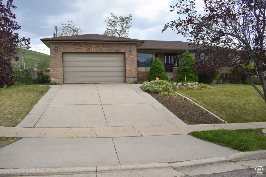 View of front facade featuring brick siding, a front lawn, an attached garage, driveway, and roof with shingles