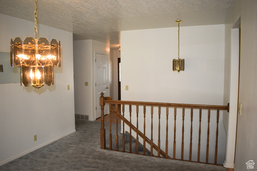 Hallway with a chandelier, carpet, a textured ceiling, and an upstairs landing