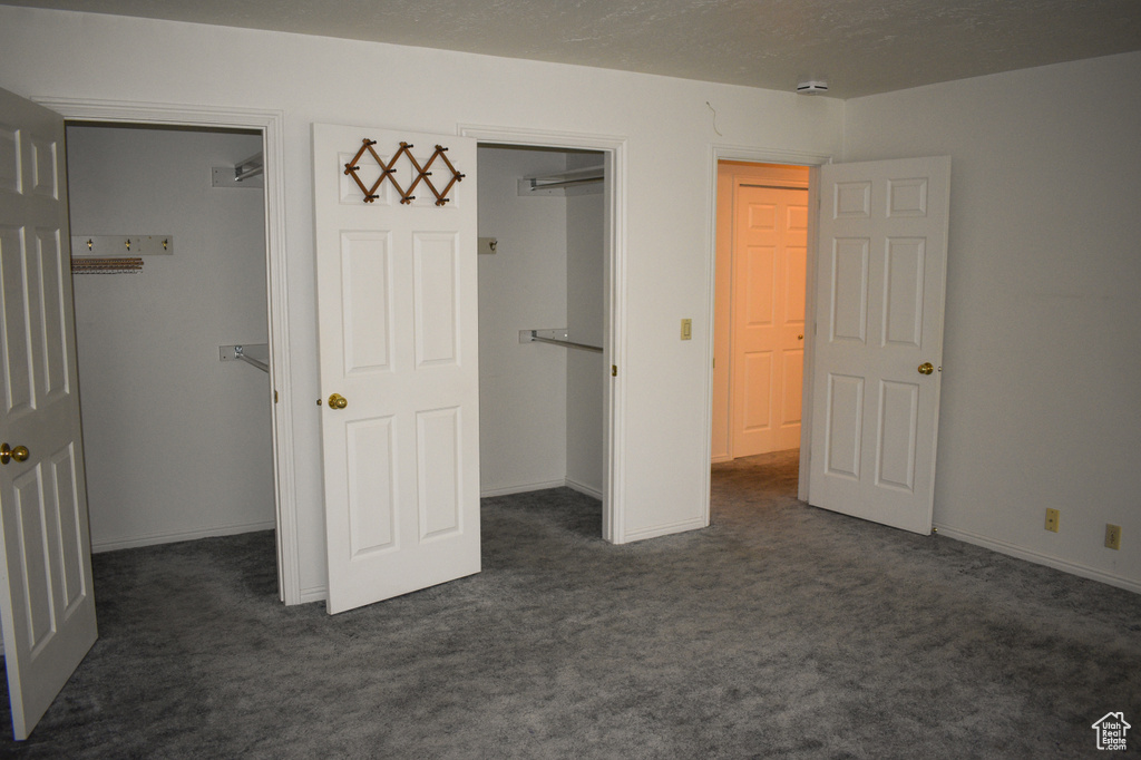 Unfurnished bedroom featuring dark colored carpet, a walk in closet, and a closet