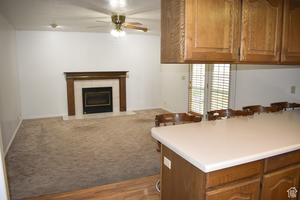 Kitchen featuring a ceiling fan, a fireplace, light carpet, brown cabinets, and light countertops