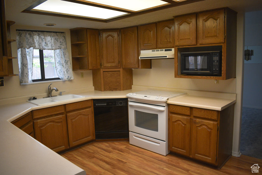 Kitchen with black appliances, under cabinet range hood, brown cabinetry, and light wood-type flooring