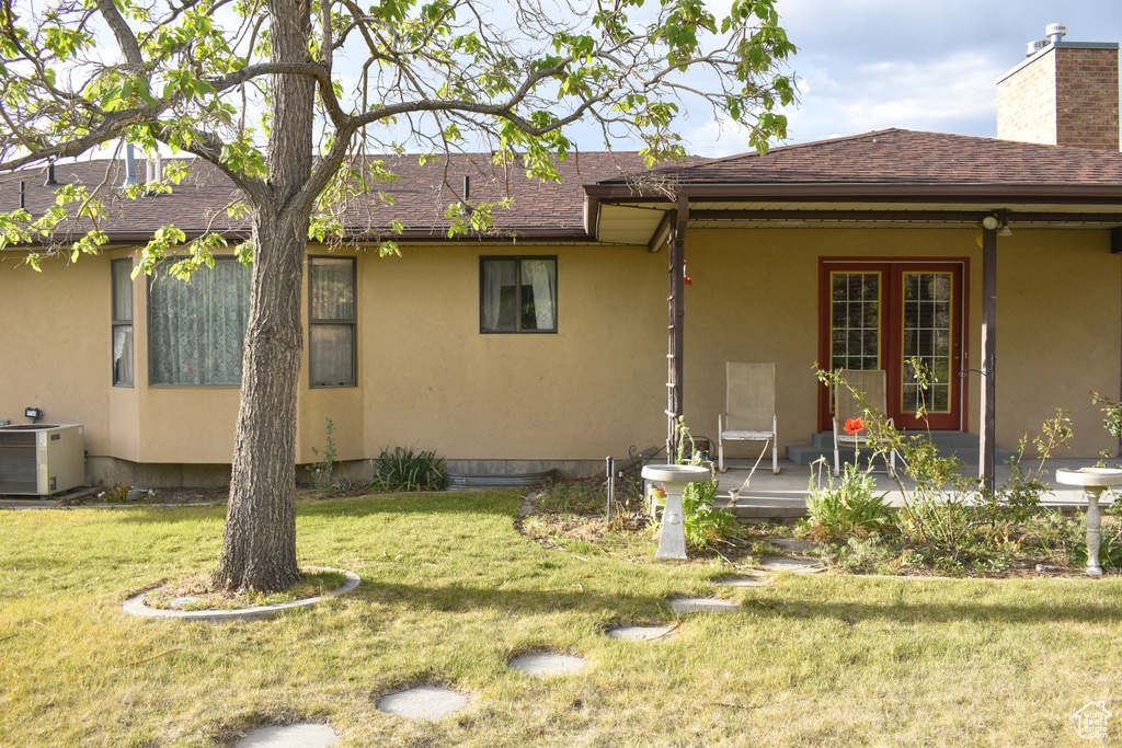 Rear view of property with stucco siding, a lawn, a shingled roof, and covered porch