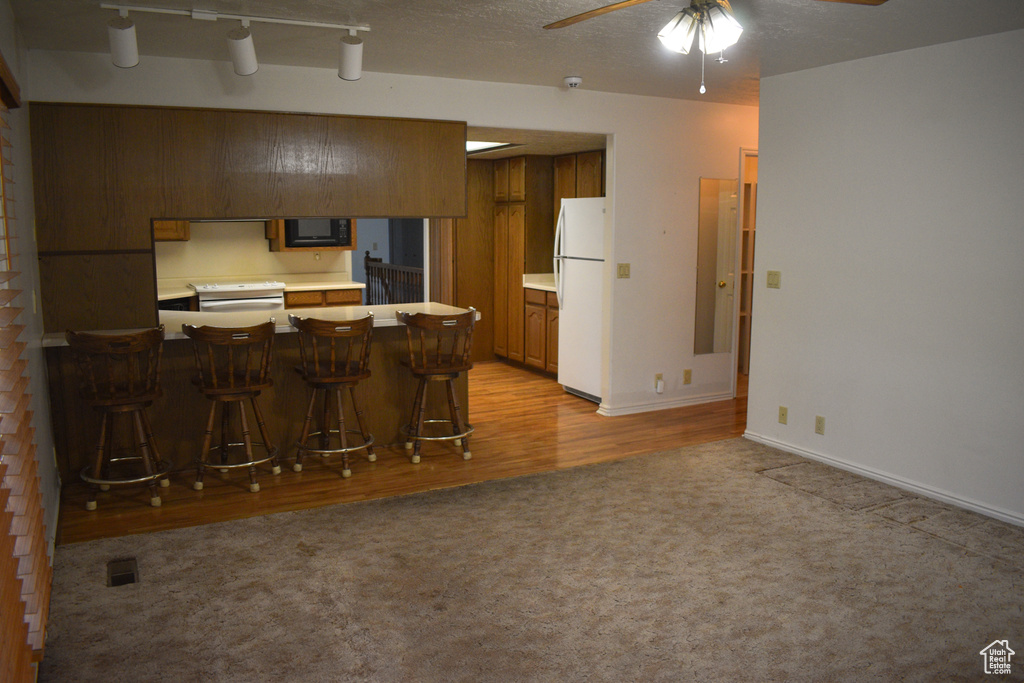 Kitchen featuring white appliances, light carpet, a peninsula, ceiling fan, and a kitchen breakfast bar