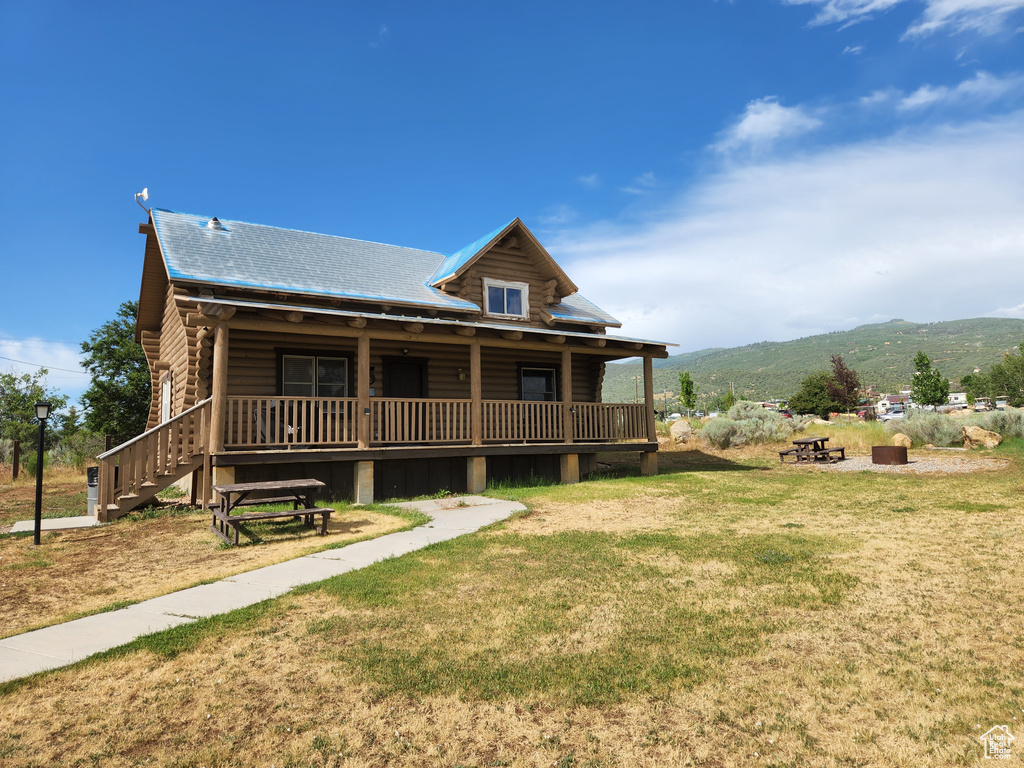 Rear view of house featuring a mountain view, covered porch, log exterior, and a lawn