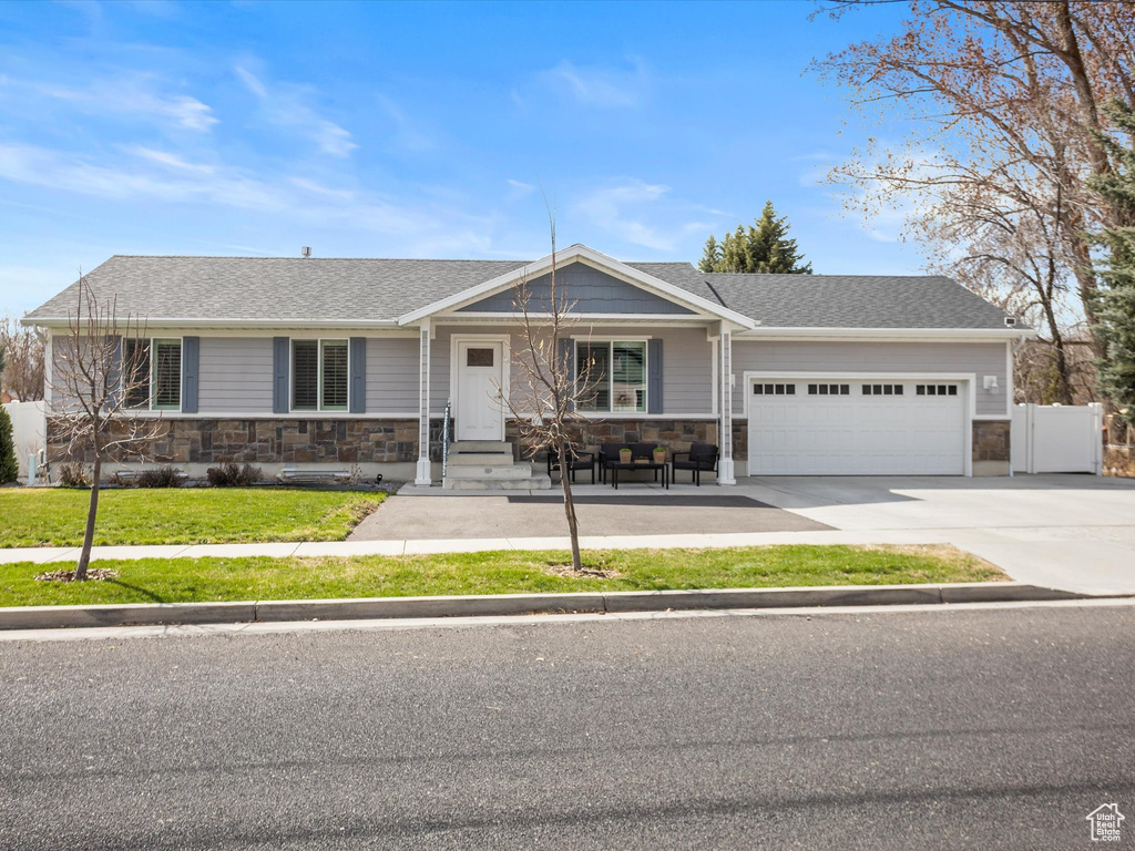 Ranch-style home featuring a front yard, driveway, stone siding, and a garage