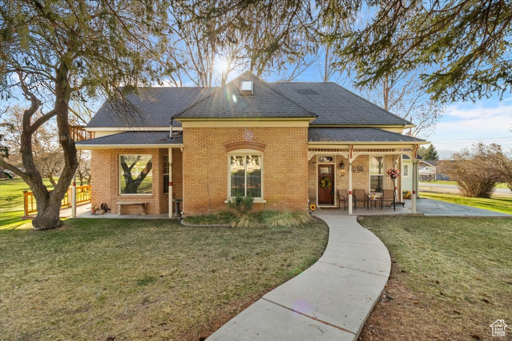 View of front of house featuring brick siding, a front yard, covered porch, and roof with shingles