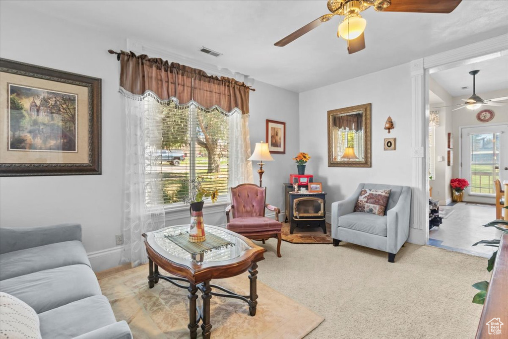 Carpeted living area with a wood stove, ceiling fan, visible vents, and baseboards