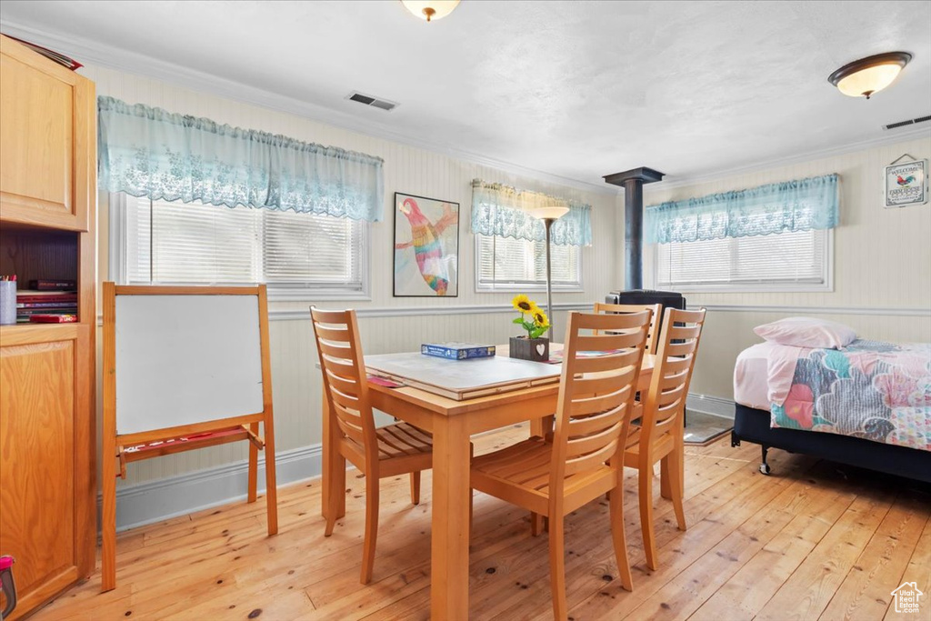 Dining room with light wood-style floors, a wood stove, crown molding, and visible vents
