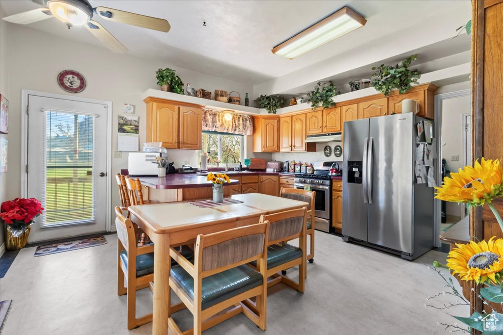 Kitchen with concrete flooring, a ceiling fan, appliances with stainless steel finishes, under cabinet range hood, and a sink