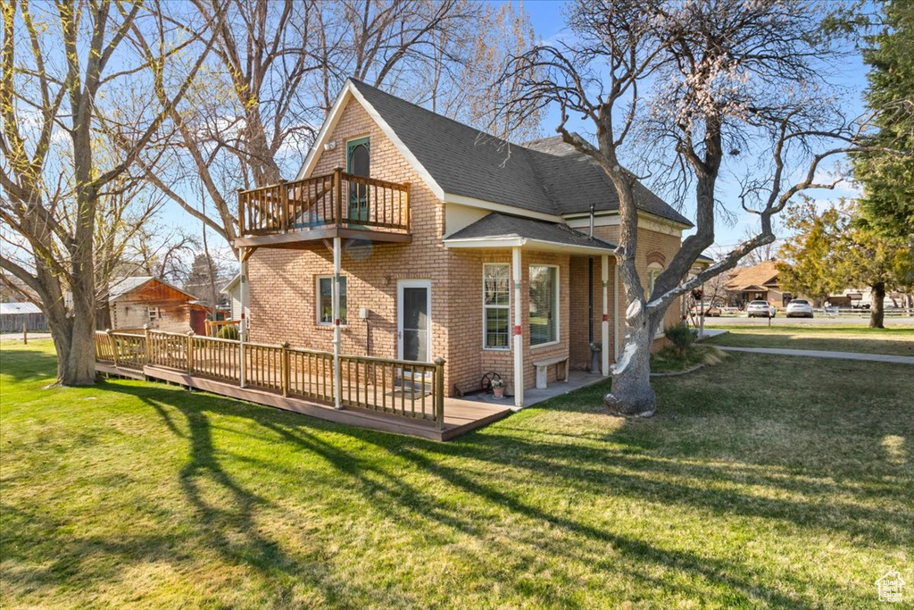 Rear view of house featuring a yard, a balcony, brick siding, a wooden deck, and roof with shingles