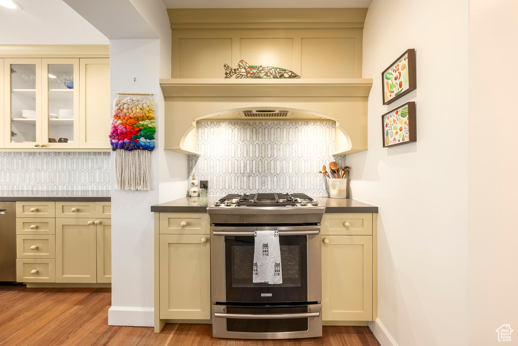 Kitchen featuring glass insert cabinets, backsplash, stainless steel range with gas cooktop, and light wood-style flooring