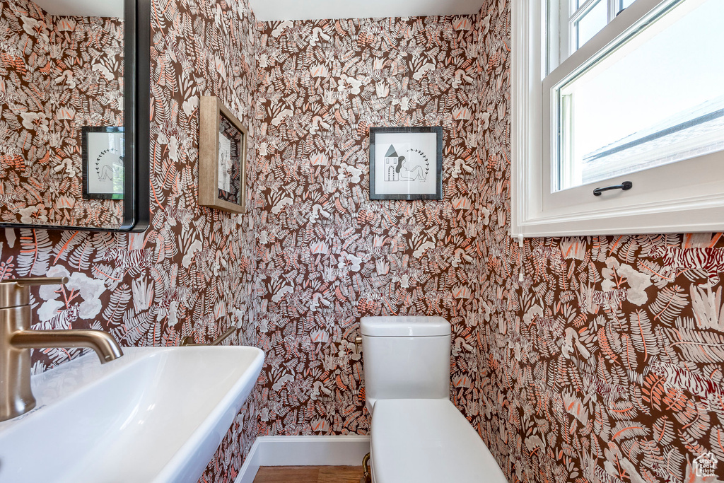 Bathroom featuring a sink, toilet, wallpapered walls, and baseboards
