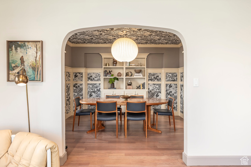 Dining room with crown molding, arched walkways, and light wood-style flooring