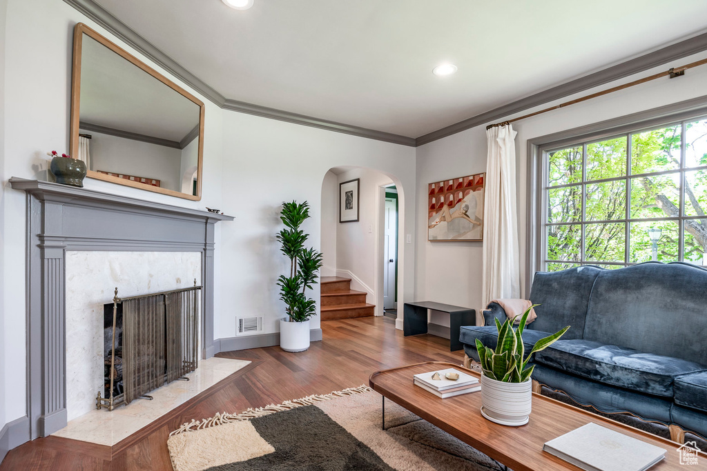 Living area featuring arched walkways, wood finished floors, ornamental molding, recessed lighting, and a premium fireplace