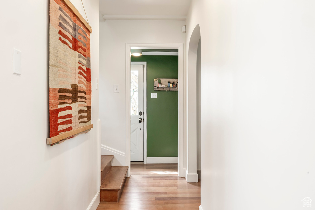 Hall with arched walkways, baseboards, stairs, and wood finished floors
