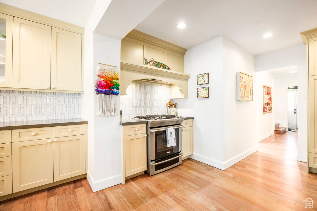 Kitchen featuring light wood-style flooring, stainless steel range with gas cooktop, baseboards, cream cabinetry, and backsplash