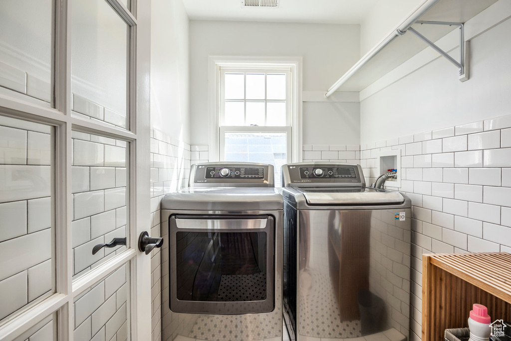Washroom featuring visible vents, wainscoting, tile walls, cabinet space, and independent washer and dryer