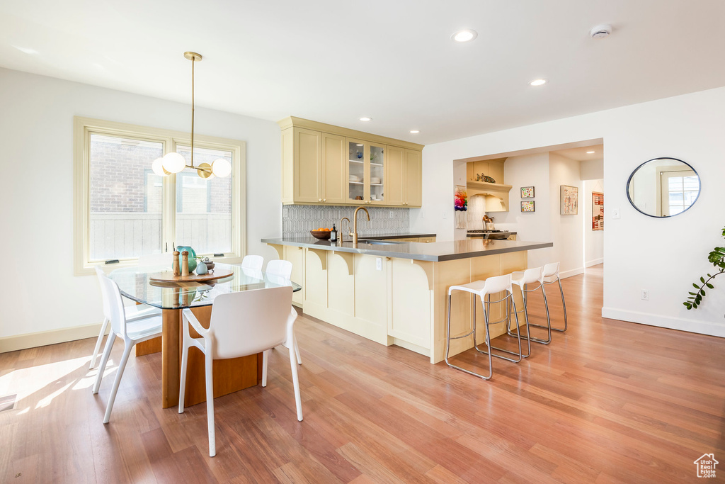 Kitchen featuring light wood finished floors, a breakfast bar area, a peninsula, recessed lighting, and glass insert cabinets