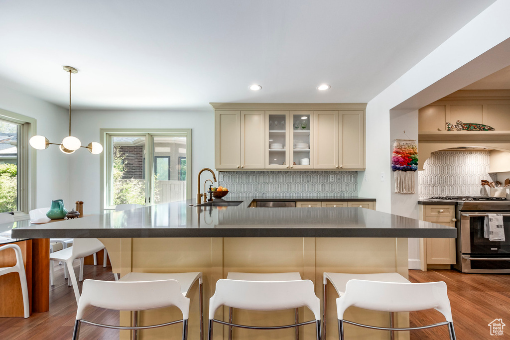 Kitchen with gas stove, a sink, dark countertops, cream cabinetry, and a kitchen bar