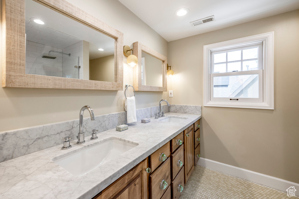Bathroom featuring double vanity, recessed lighting, tiled shower, and baseboards
