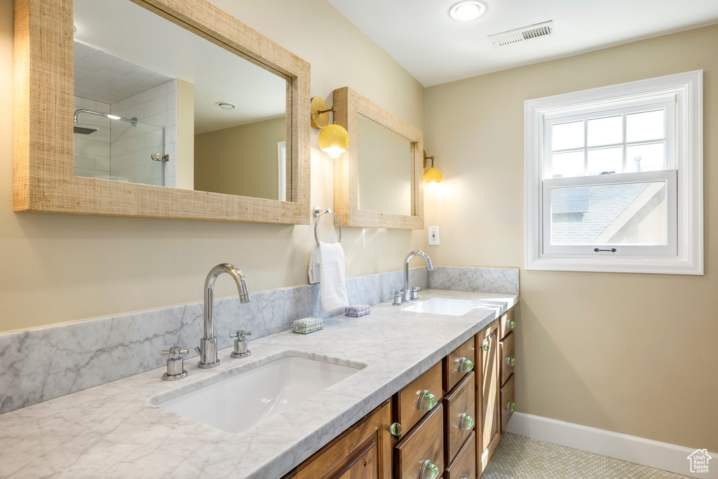 Bathroom with visible vents, a sink, double vanity, and tiled shower