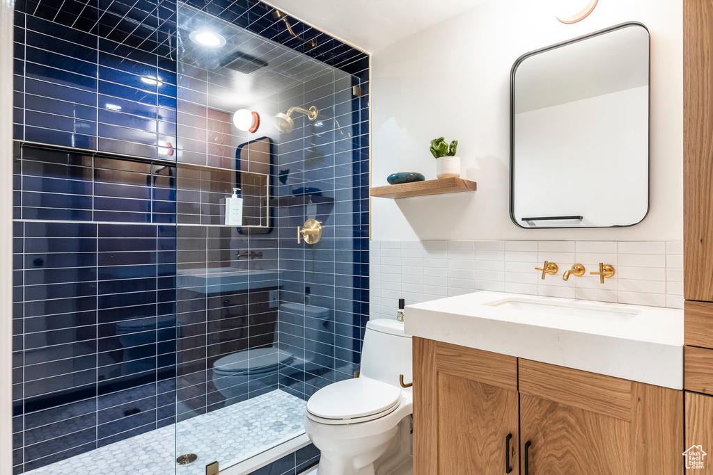 Bathroom with vanity, toilet, tiled shower, and tile walls