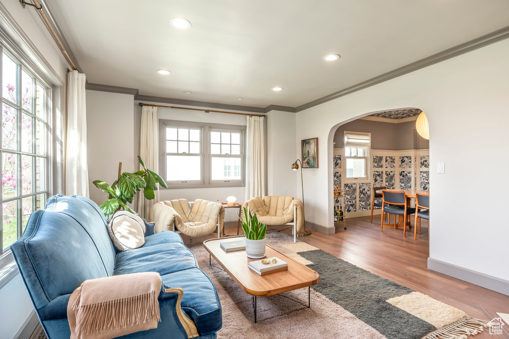 Living room with arched walkways, baseboards, light wood-style floors, ornamental molding, and recessed lighting