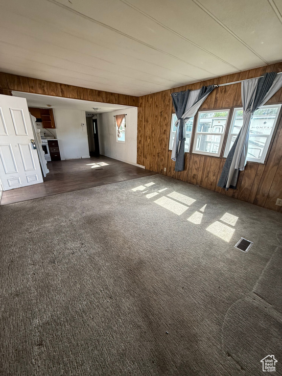 Unfurnished living room featuring wooden walls and carpet flooring