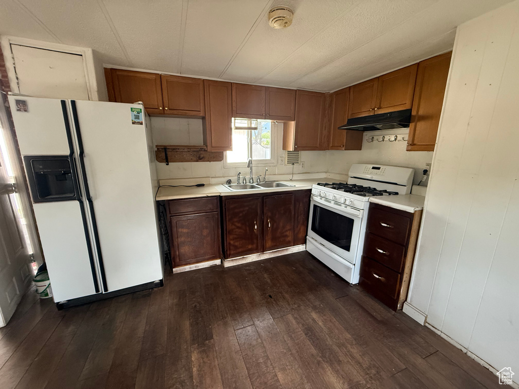 Kitchen featuring white appliances, a sink, under cabinet range hood, dark wood-style floors, and light countertops