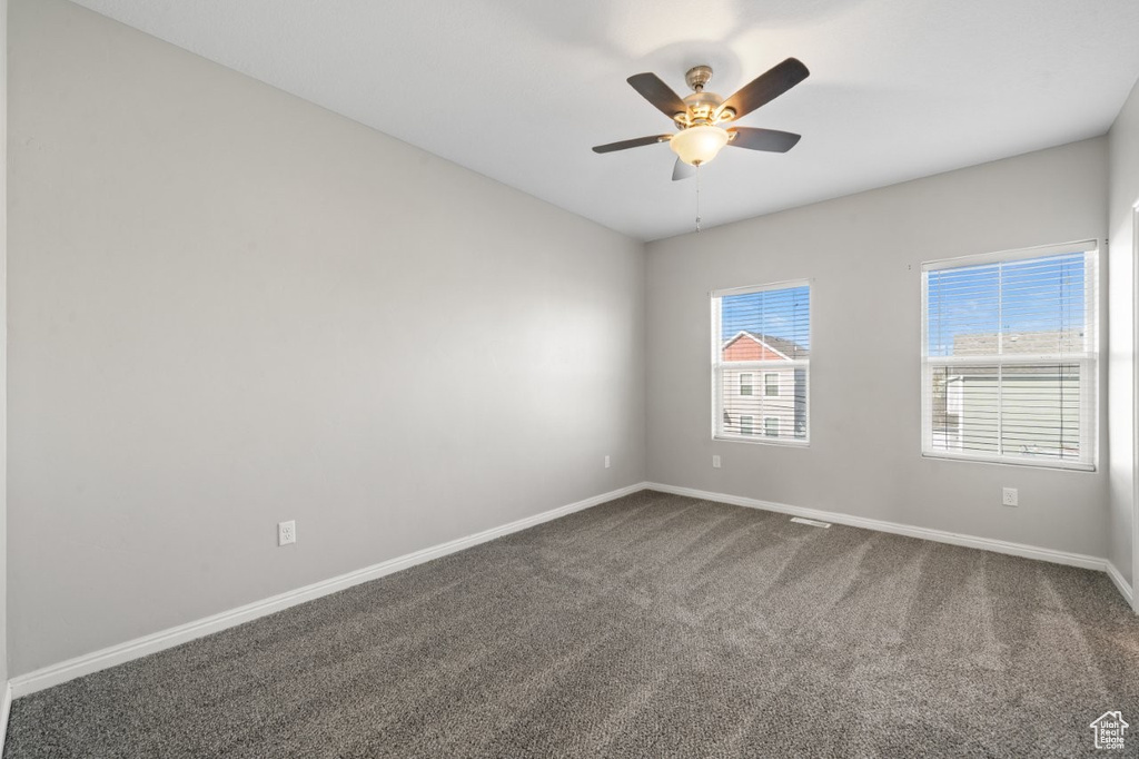 Spare room featuring baseboards, dark carpet, and a ceiling fan