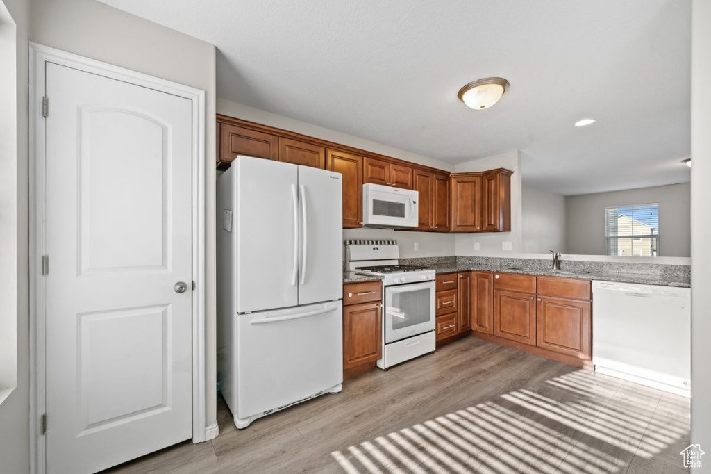 Kitchen featuring white appliances, light wood-style flooring, brown cabinetry, stone countertops, and a sink