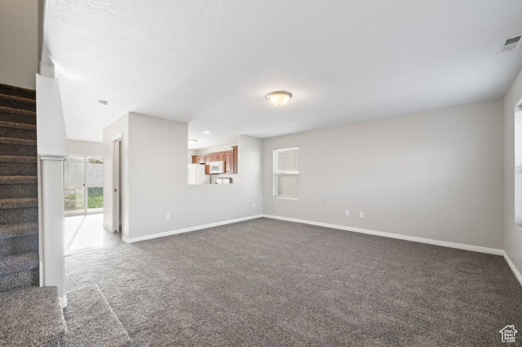 Unfurnished living room featuring dark carpet, baseboards, stairway, and visible vents