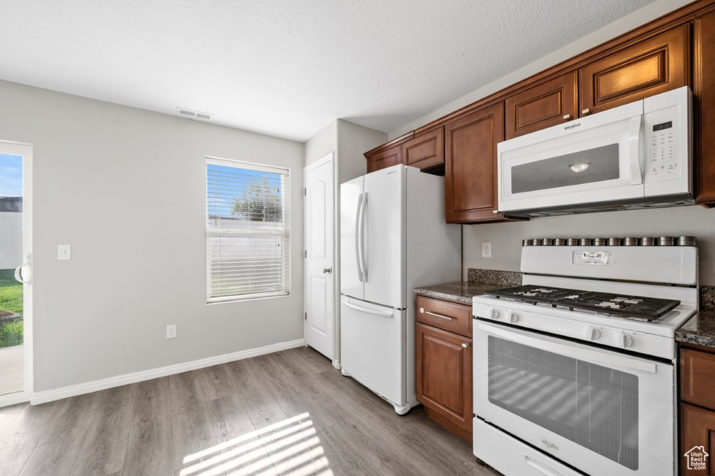 Kitchen featuring baseboards, white appliances, visible vents, brown cabinets, and light wood finished floors