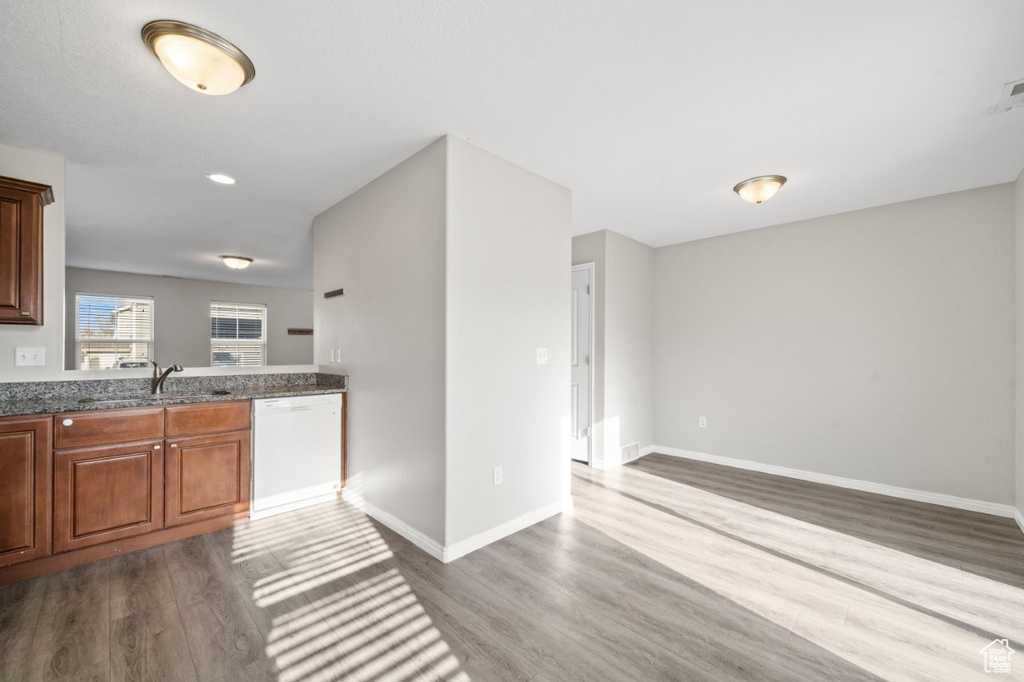 Kitchen featuring dark stone countertops, baseboards, dishwasher, a sink, and dark wood-style floors