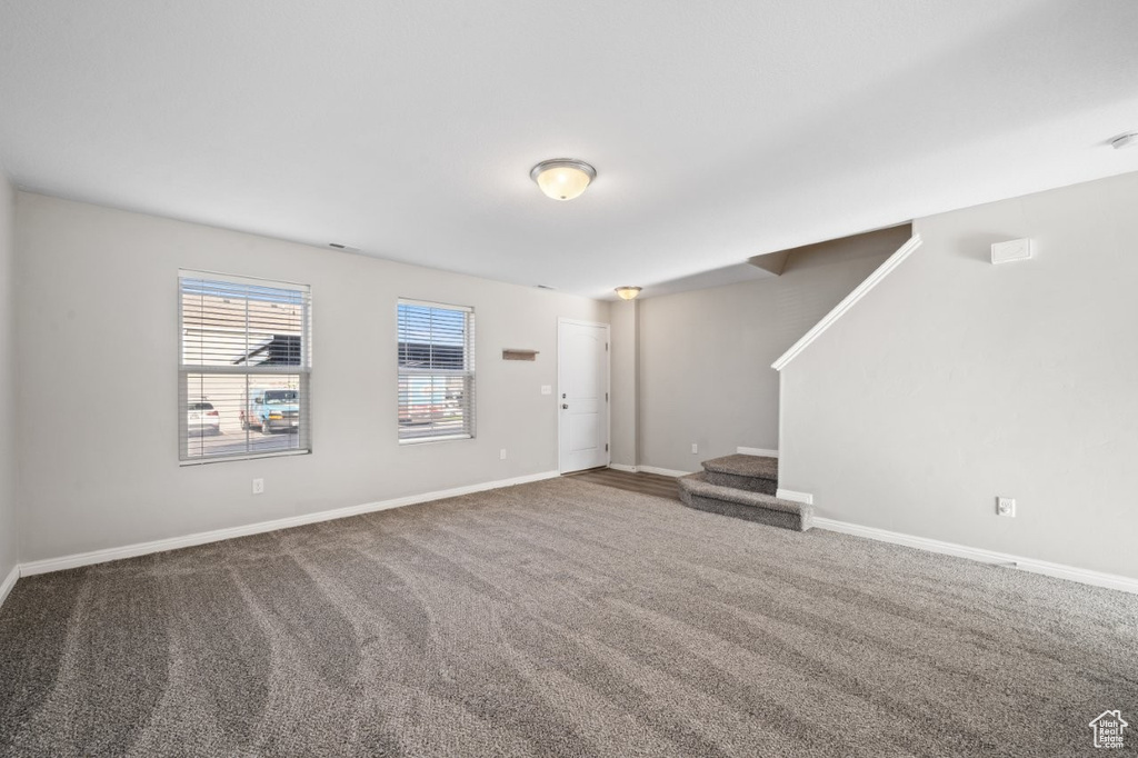 Unfurnished living room featuring carpet floors, baseboards, and stairs
