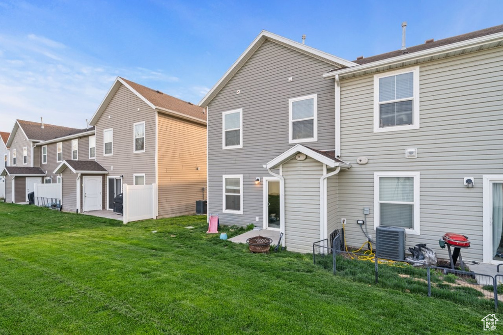 Back of house with central AC, an outdoor fire pit, fence, and a lawn
