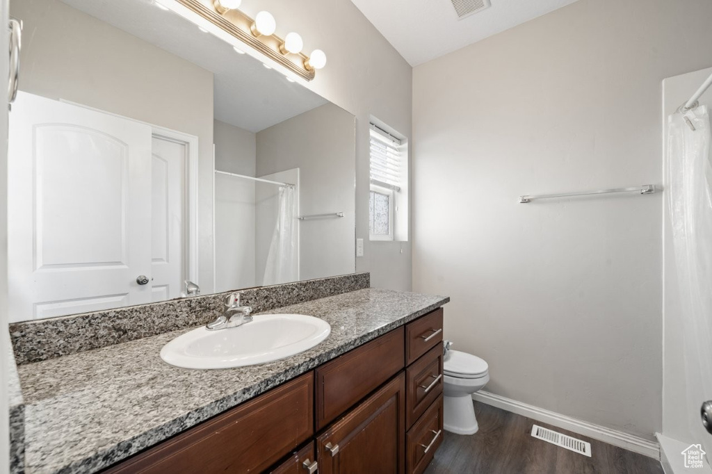 Bathroom featuring visible vents, baseboards, toilet, vanity, and wood finished floors
