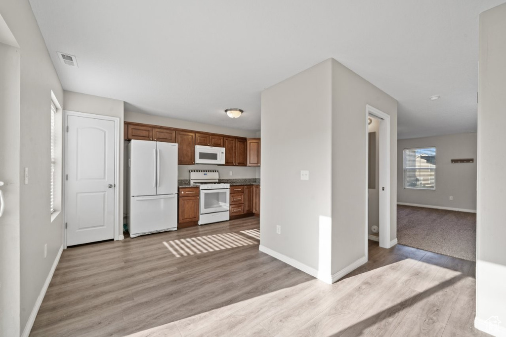 Kitchen with light wood-style floors, white appliances, visible vents, and baseboards