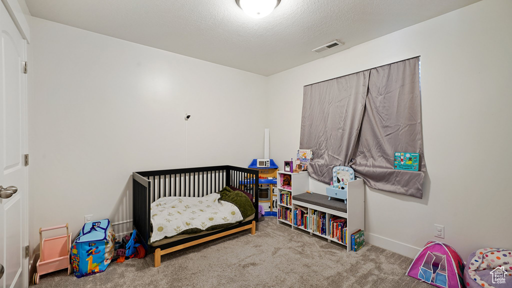 Carpeted bedroom featuring a textured ceiling, baseboards, visible vents, and a crib