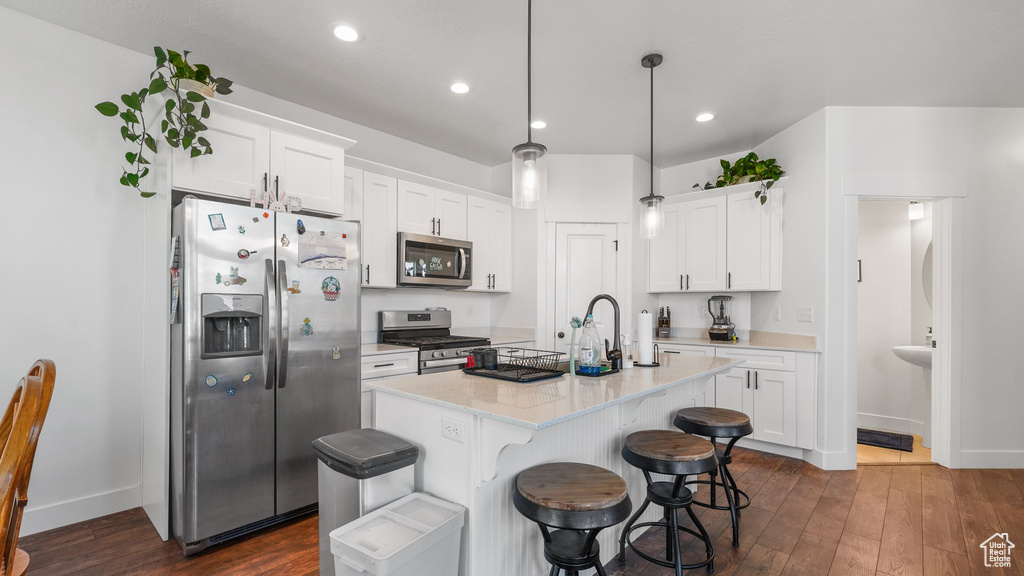 Kitchen featuring stainless steel appliances, dark wood-style flooring, white cabinets, and a center island with sink