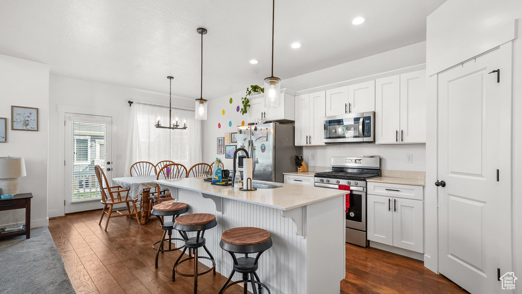 Kitchen with dark wood-style flooring, appliances with stainless steel finishes, an island with sink, a kitchen bar, and white cabinetry