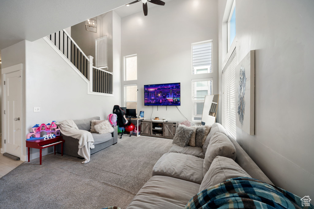 Living area featuring a high ceiling, a ceiling fan, carpet, and stairway
