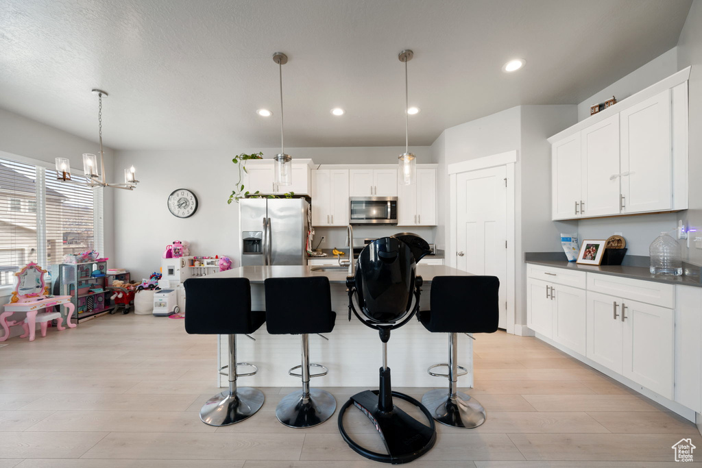 Kitchen featuring dark countertops, light wood-type flooring, appliances with stainless steel finishes, and a kitchen bar