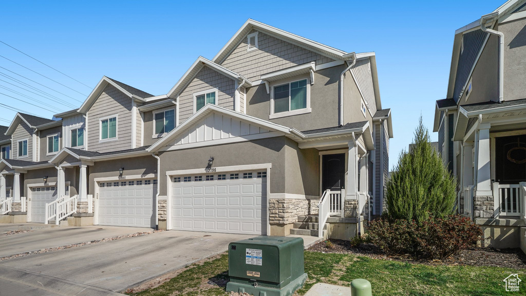 View of front of house with stone siding, a garage, board and batten siding, concrete driveway, and stucco siding