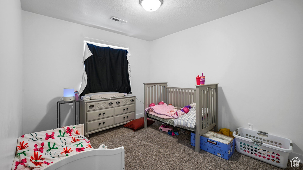 Carpeted bedroom with a crib, visible vents, and a textured ceiling