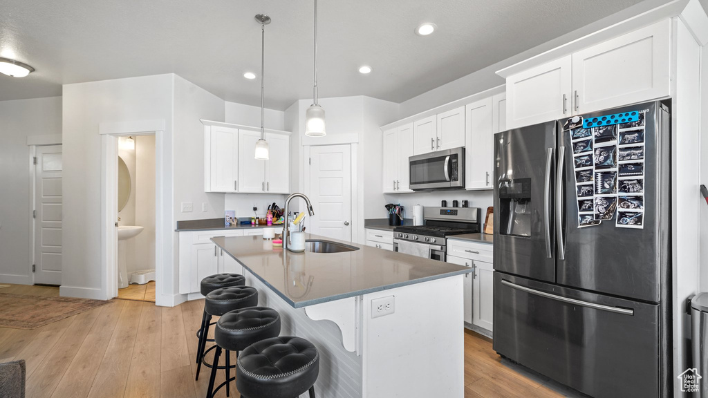 Kitchen with a kitchen bar, appliances with stainless steel finishes, light wood finished floors, and a sink